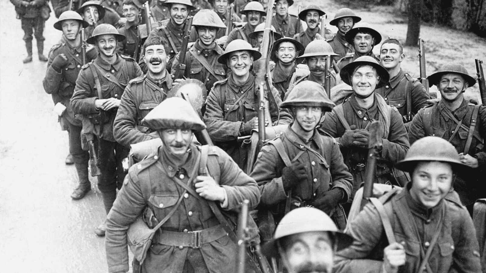A historical black-and-white photograph showing a large, dense column of smiling British soldiers from the 10th Battalion, Royal Fusiliers, marching forward during World War I. The infantrymen are all wearing standard wool uniforms, webbing equipment, and steel Brodie helmets, with many carrying rifles slung over their shoulders. Most of the men are looking directly at the camera with wide grins and expressions of high morale as they move along an outdoor road.