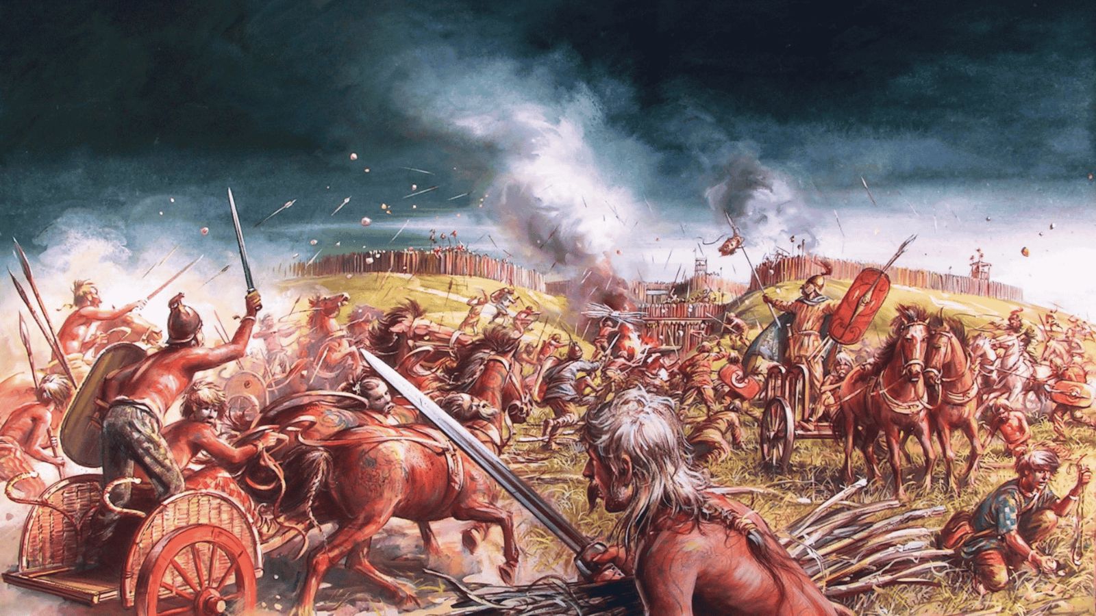 An action-packed historical illustration depicting an Iron Age Celtic battle in Britain, focused on an assault against a fortified hillfort. In the foreground, Celtic warriors with long hair and bare torsos operate two-wheeled wooden chariots drawn by galloping horses, with one fighter raising a sword aloft. In the center, infantrymen clash in chaotic hand-to-hand combat beneath a smoke-filled sky, while other fighters on the right charge forward on horseback and in chariots. In the background, defenders line the top of a wooden palisade wall along the grassy hill, raining down stones and projectiles onto the attackers below.